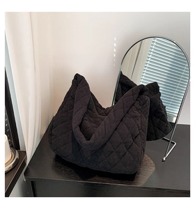 Detail of black quilted corduroy tote bag showing soft texture on a wooden table