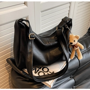Detalle del bolso tote negro en cuero granulado con hebillas doradas y colgante de osito