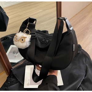 Detail of black nylon dumpling bag with adjustable strap and owl plush charm
