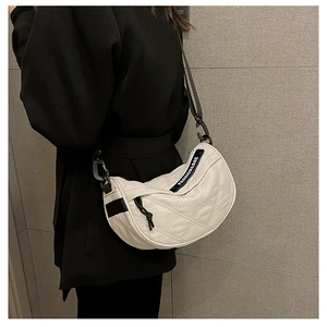 Close-up of white quilted half-moon saddle bag featuring black adjustable strap detail