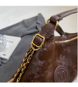 Close-up of deep brown matte leather tote bag with gold buckle and embossed M logo detail