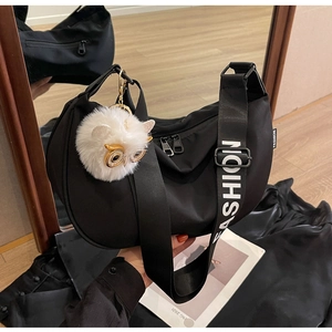 Detail of black nylon crescent bag featuring a wide 'FASHION' strap and plush owl charm