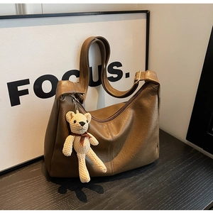 Detalle de bolso tote marrón de cuero con un colgante de oso tejido en madera