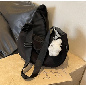 Detail of black nylon crescent bag featuring a fashion label and plush bear charm