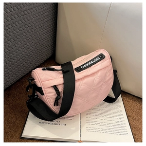 Detail of light pink quilted saddle bag with black adjustable wide strap on a book