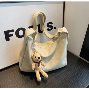 Detalle del bolso hobo crema con colgante de oso tejido y hebilla metálica elegante