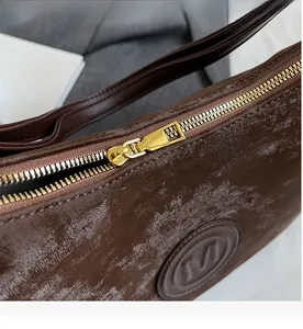 Detail of smooth gold zipper and embossed M logo on dark brown marble textured tote bag