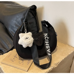 Detail view of black nylon crescent bag with branded logo strap and cute bear charm