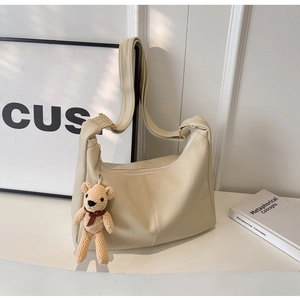 Primer plano del bolso hobo beige de cuero PU con un adorable colgante de oso de punto