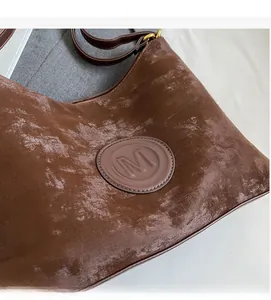 Detailed macro view of the brown velvet texture and leather M logo patch with gold buckle