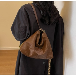 Close-up of brown vintage leather shoulder bag with M logo and golden chain details