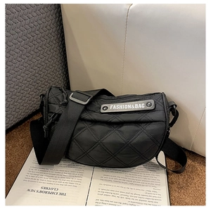 Detail of black quilted nylon crossbody bag with adjustable wide strap on a soft sofa