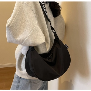 Detail view of black crescent crossbody bag featuring a branded strap and white plush charm