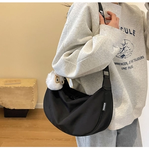 Detail of black nylon crescent bag with wide strap and cute white owl plush charm