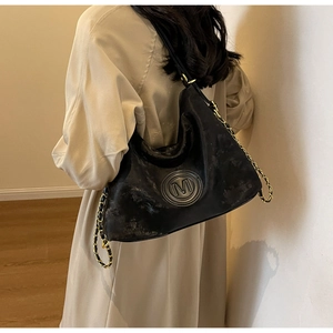 Detail of black vintage tote bag featuring a metallic M logo and chain strap on a model