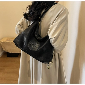Detail of black vintage leather tote bag with gold chain strap and metal M logo