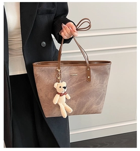 Detail of vintage brown tote bag with metal plaque, textured leather and plush bear charm