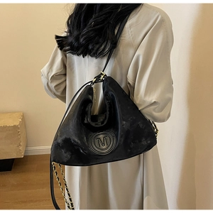 Detail of a pleated black crossbody bag with gold chain strap and metal 'M' logo