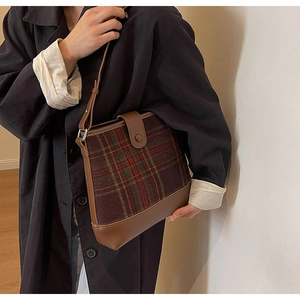 Sac seau à carreaux marron avec garniture en cuir porté sur un trench-coat noir d'automne