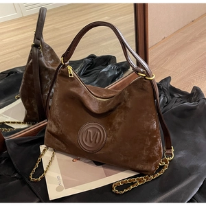 Detail view of brown leather tote bag with M logo and gold chain strap on black silk fabric