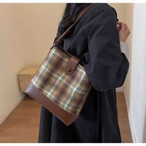 Détail d'un sac seau à carreaux vert et marron sur manteau noir avec anses en cuir