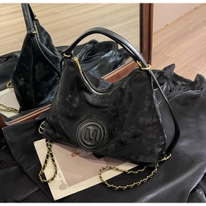 Detail of black moon-shaped Hobo bag with M logo, gold chain strap and velvet texture