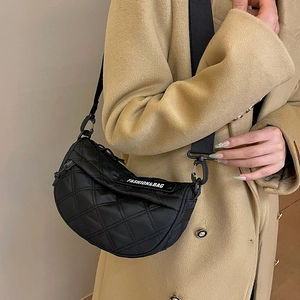 Black quilted crescent crossbody bag with wide strap worn over a camel wool coat
