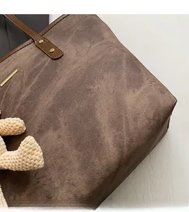 Close-up of brown tote bag featuring textured fabric, metal rivets, and knit teddy bear charm