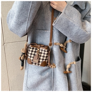 Brown and beige checkerboard crossbody bucket bag shown with a grey winter coat