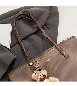 Detail of vintage brown leather tote bag featuring a cute beige knitted bear charm