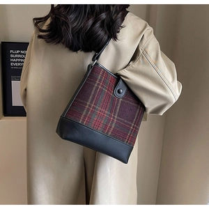 Détail du sac seau à carreaux rouge et noir porté avec un trench-coat beige chic