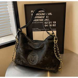 Detail of vintage black hobo bag with embossed M logo and gold chain strap on a table