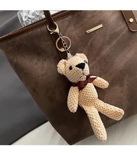 Detail of a beige knitted bear bag charm with a brown bow and gold metal keychain