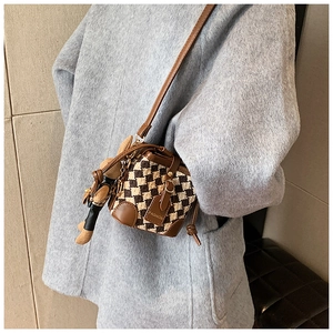 Brown checkered crossbody bucket bag with plush charm on stylish grey coat background