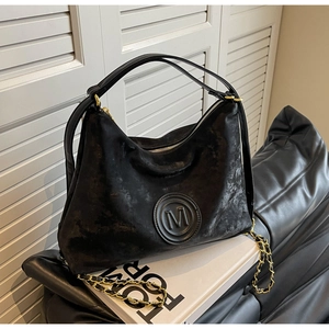 Close-up of black retro tote bag with embossed M logo and gold chain strap detail