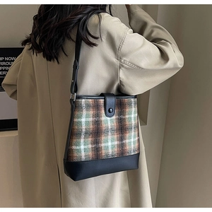 Sac seau à carreaux marron et vert porté par un mannequin en trench beige