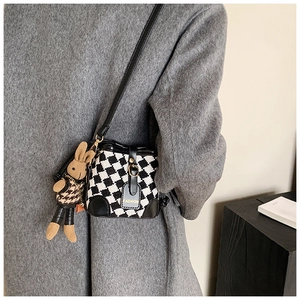 Detail of checkered crossbody bag with plush rabbit charm on wool fabric texture