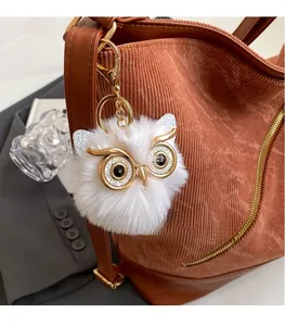 Close-up of a fluffy white owl charm with golden eyes attached to a corduroy tote bag