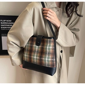 Détail du sac à bandoulière en toile à carreaux avec lanière en cuir noir sur trench