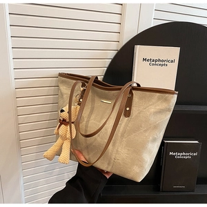Detail of a large beige tote bag with brown leather handles and a knit bear charm