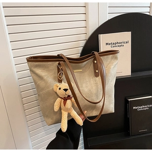 Detail of grey tote bag with brown straps, gold logo plate and cute bear charm