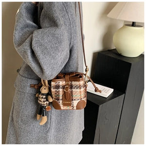 Detailed shot of retro plaid bucket bag with brown leather trim and plush bunny charm