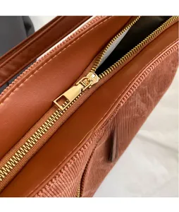 Macro shot of smooth gold-tone metal zipper and textured corduroy fabric on a tote bag