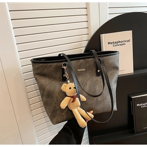 Detail of grey textured tote bag with black handles and a cute knit bear pendant