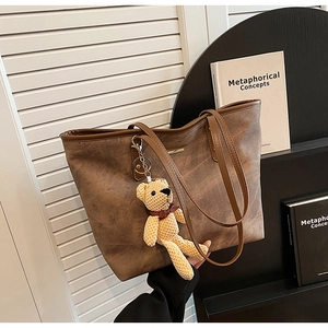 Close-up of a dark brown faux leather tote bag featuring a cute knitted teddy bear charm