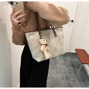 Detail of light gray tote bag with brown straps and a small woven bear pendant charm