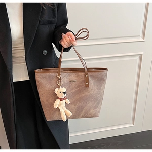 Brown frosted leather tote bag detail with minimalist metal bar and bear charm