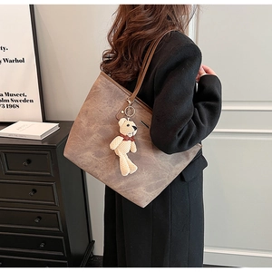 Close-up of a large vintage brown tote bag with a beige woven bear charm on a shoulder strap