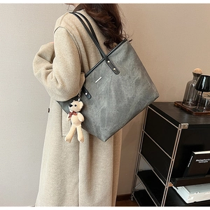Detail view of large grey tote bag with vintage texture and cute bear charm accessory
