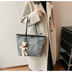 Detail of dark grey tote bag with stone texture, gold tag and cute bear pendant charm